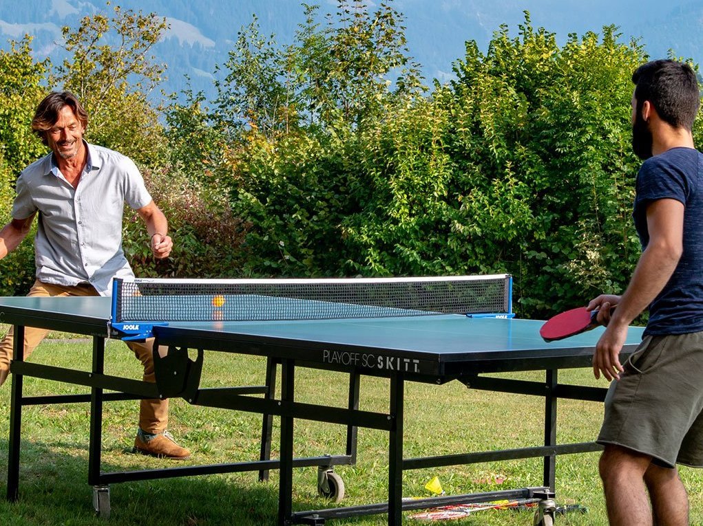 Zwei Männer spielen im Garten Tischtennis - im Hintergrund Alpenpanorama