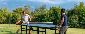 Zwei Männer spielen im Garten Tischtennis - im Hintergrund Alpenpanorama