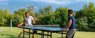 Zwei Männer spielen im Garten Tischtennis - im Hintergrund Alpenpanorama