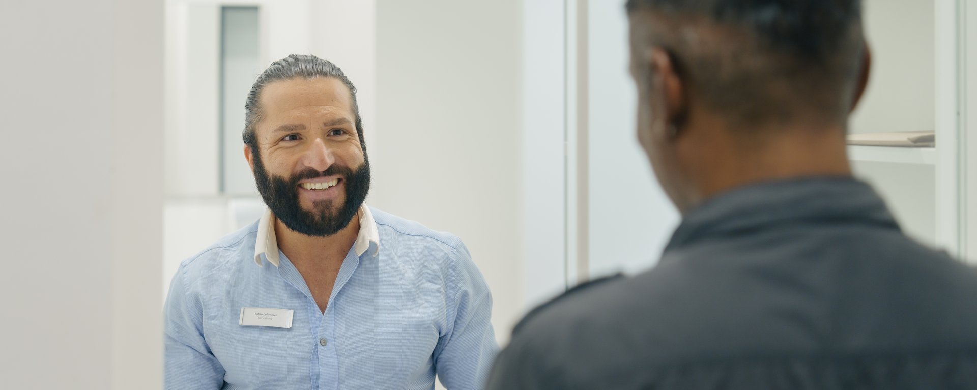 Ein Mann arbeitet an der Kasse und laechelt seinen Kunden an