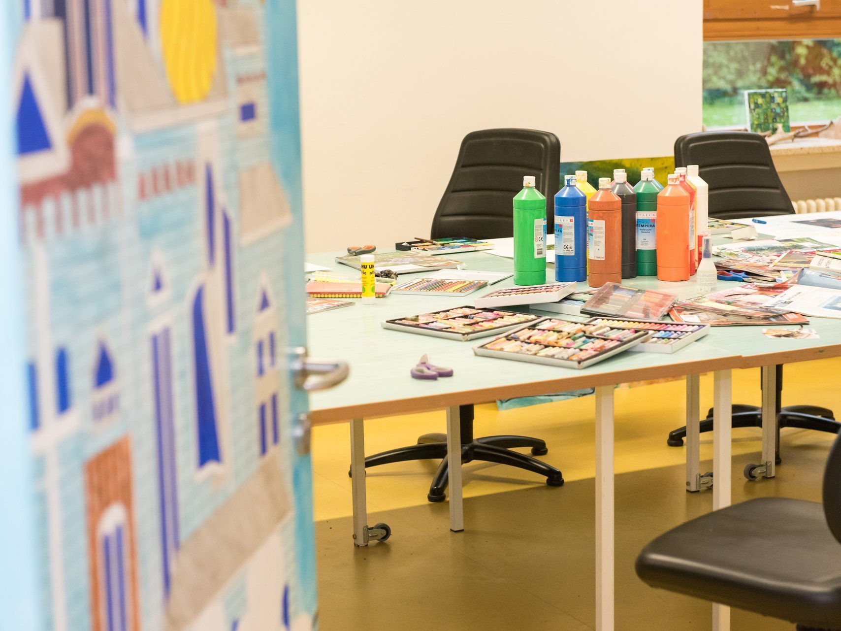 Kreativraum: auf einem Tisch stehen Farbflaschen und unzälig Stifte, sowie Zeitschriften und Papier