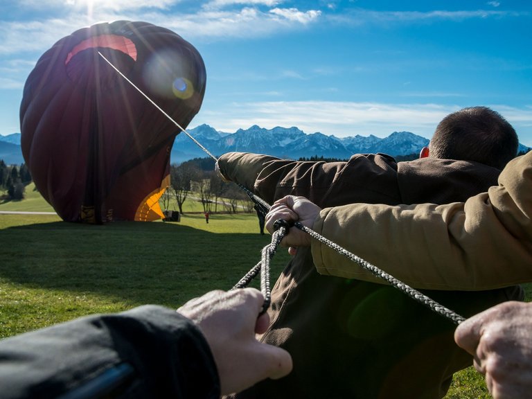 Männer helfen auf einer Wiese einen Heißluftballon aufzurichten - halten ein Seil