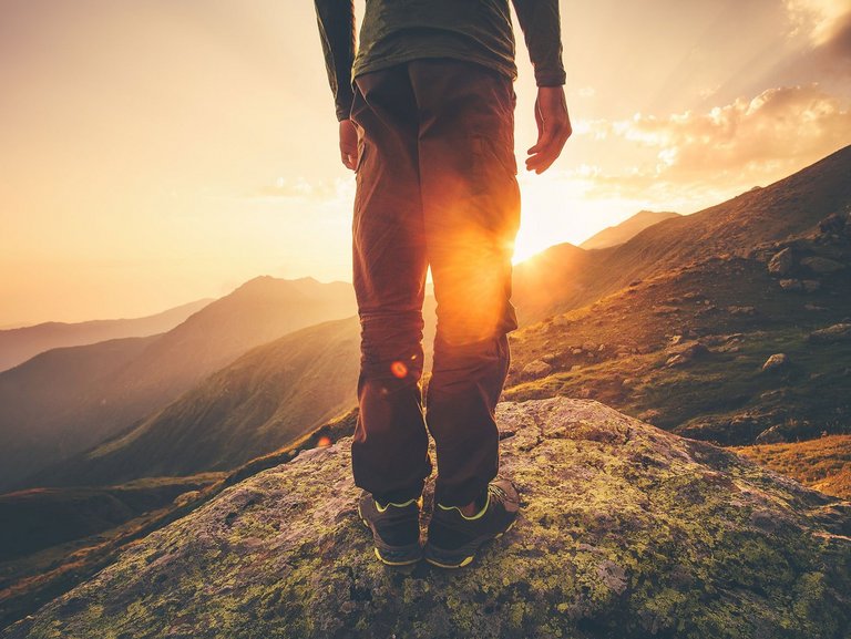 Symbolbild: ein Mann im Trekking-Outfit steht auf einem Berg - Die Sonne geht auf