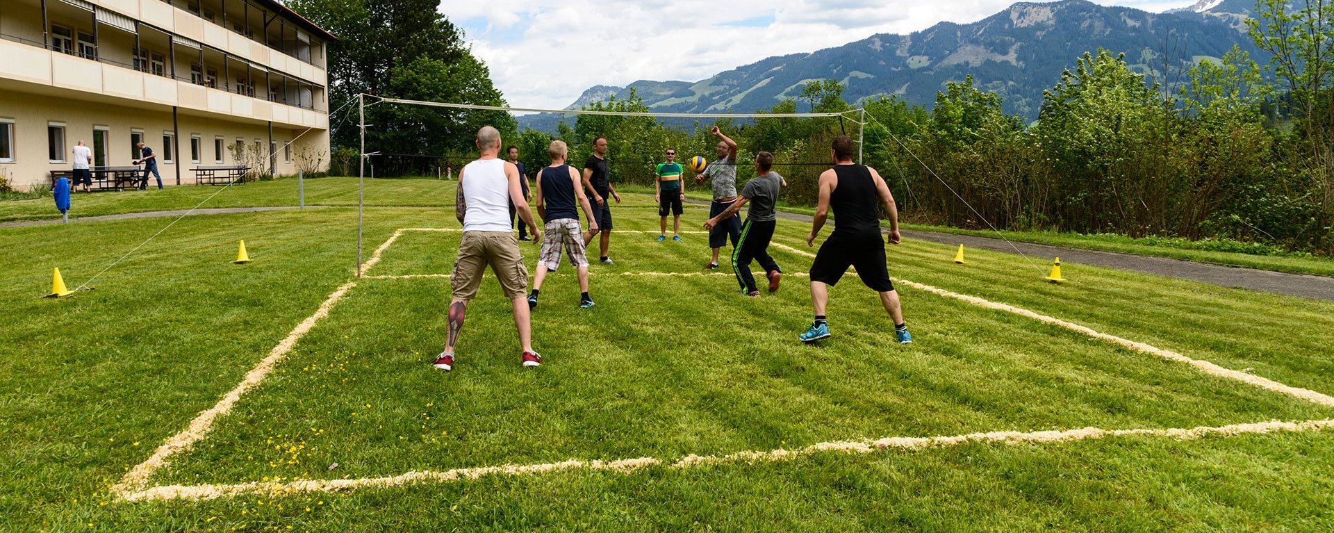 Volleyball auf der Wiese - am Netz stehen zwei Manschaften - im Hintergrund Alpen